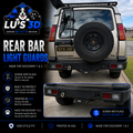 Rear bar light guards by Lu's 3D shown installed on the rear bumper of a beige Discovery 2, with a product inset showing the black metal guard pieces and marketing text on the left.